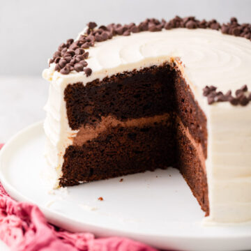 cut open chocolate cake with vanilla frosting on a white plate on top of a pink linen on a white marble surface