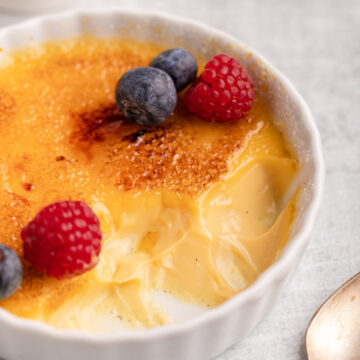 salted caramel creme brulee with a few bites taken out next to a bowl of berries