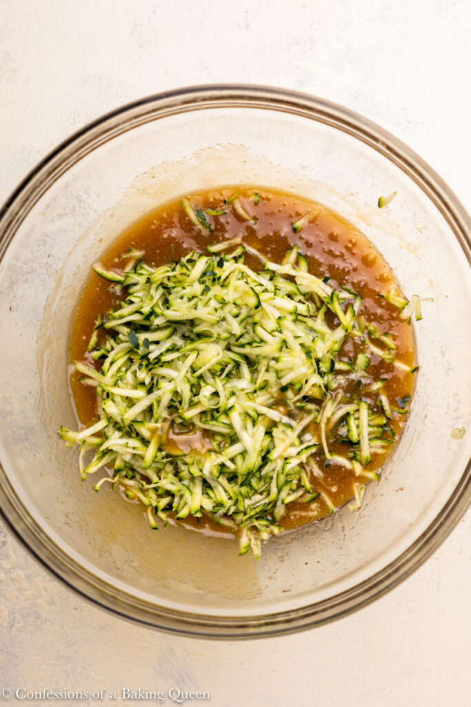shredded zucchini added to wet ingredients in a glass bowl