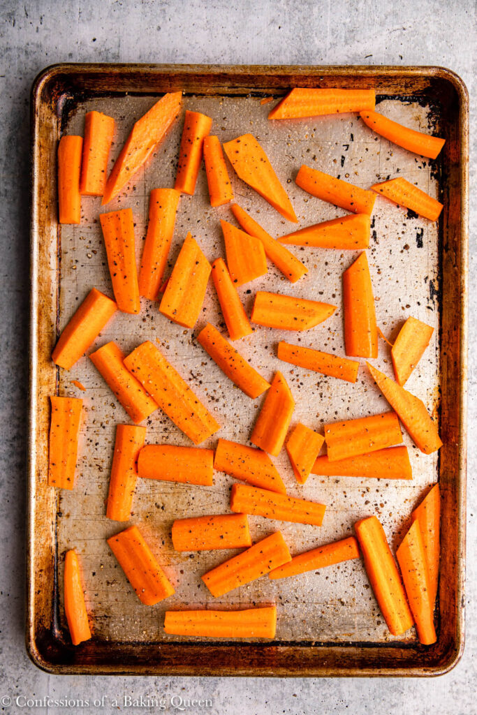 carrot pieces tossed in oil with salt and pepper on a baking sheet on a grey surface