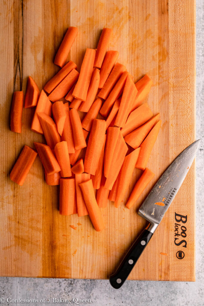 carrots sliced into thick sticks on a wood cutting board with a knife on a grey surface (