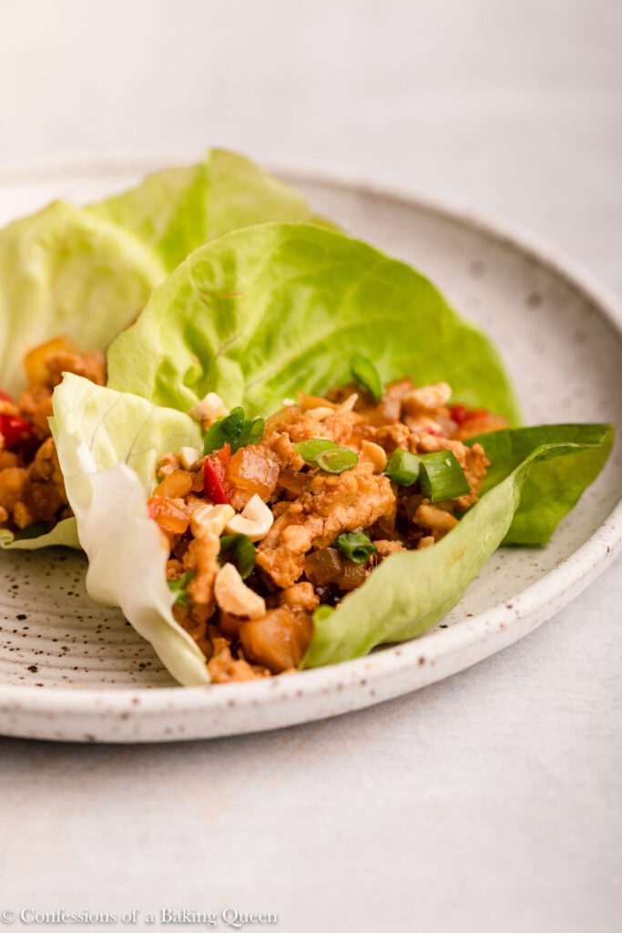 close up of chicken lettuce cups on a white and brown speckled plate on a grey surface
