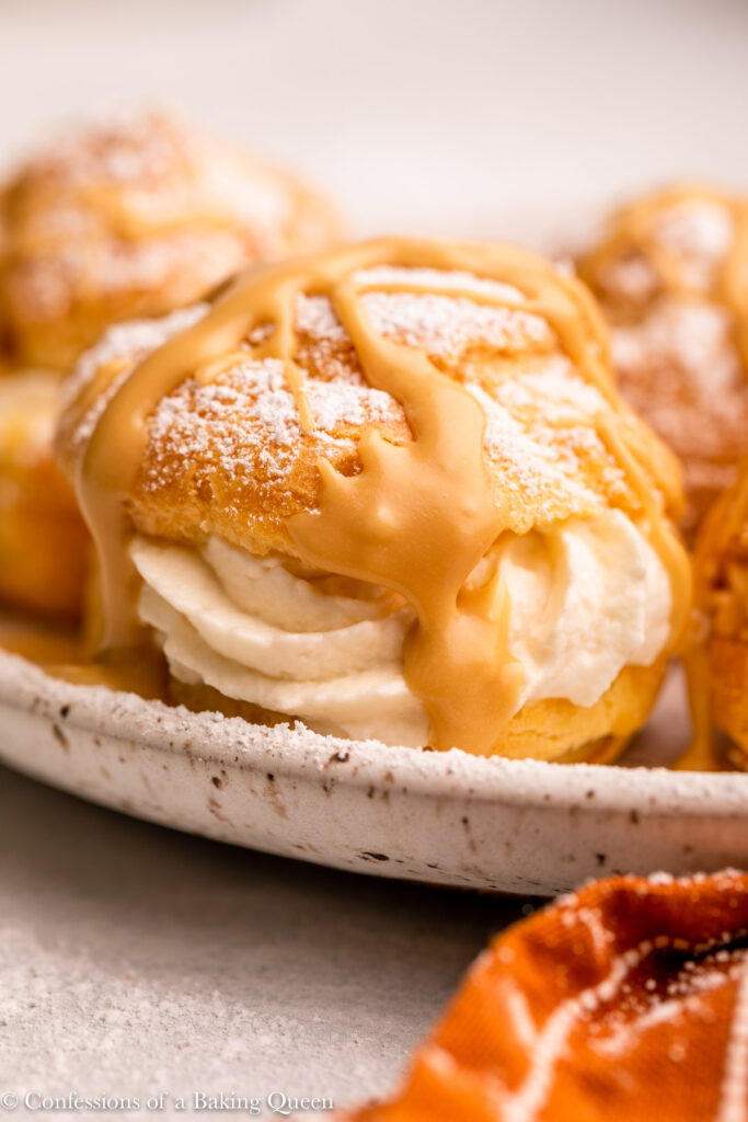 coffee drizzle cream puffs on a white speckled plate next to an orange linen