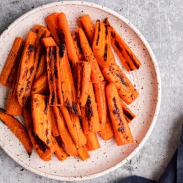 roasted carrots on white and brown speckled plate on a grey surface with a navy blue linen