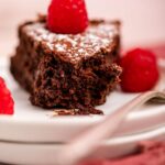 flourless chocolate cake on a white plate with raspberries and a fork