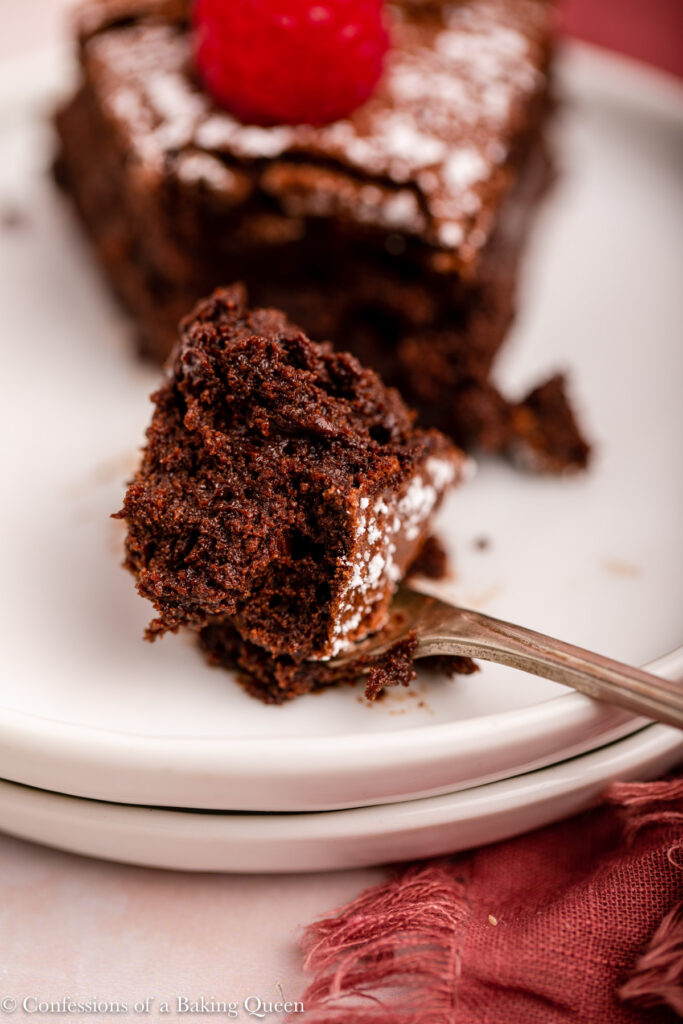 fork holding a bite of flourless chocolate cake on a white plate