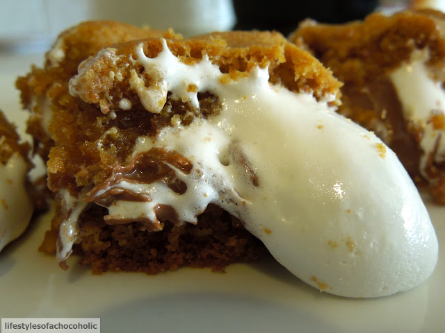 close up of s'mores cookie bar with oozing marshmallow sitting on a white plate