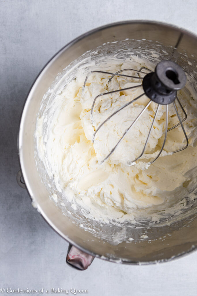 Cream Cheese Whipped Cream Frosting in a metal bowl with a wire whisk on a grey surface