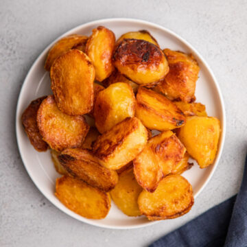 english roast potatoes on a white plate on top of a navy blue linen on a grey surface
