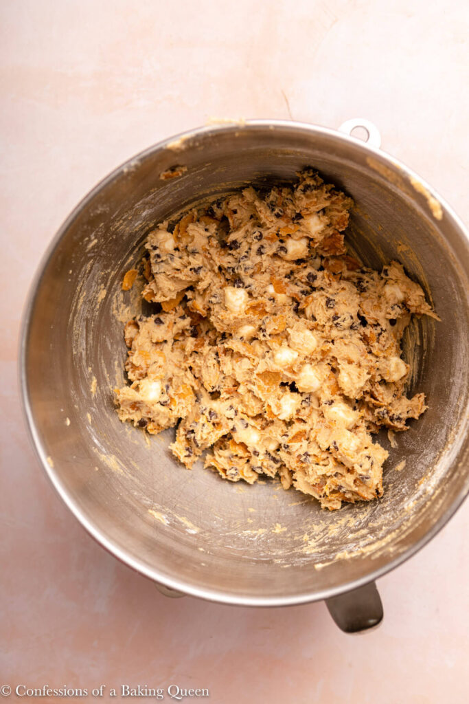 cornflake cookie dough in a metal mixing bowl on a pink surface