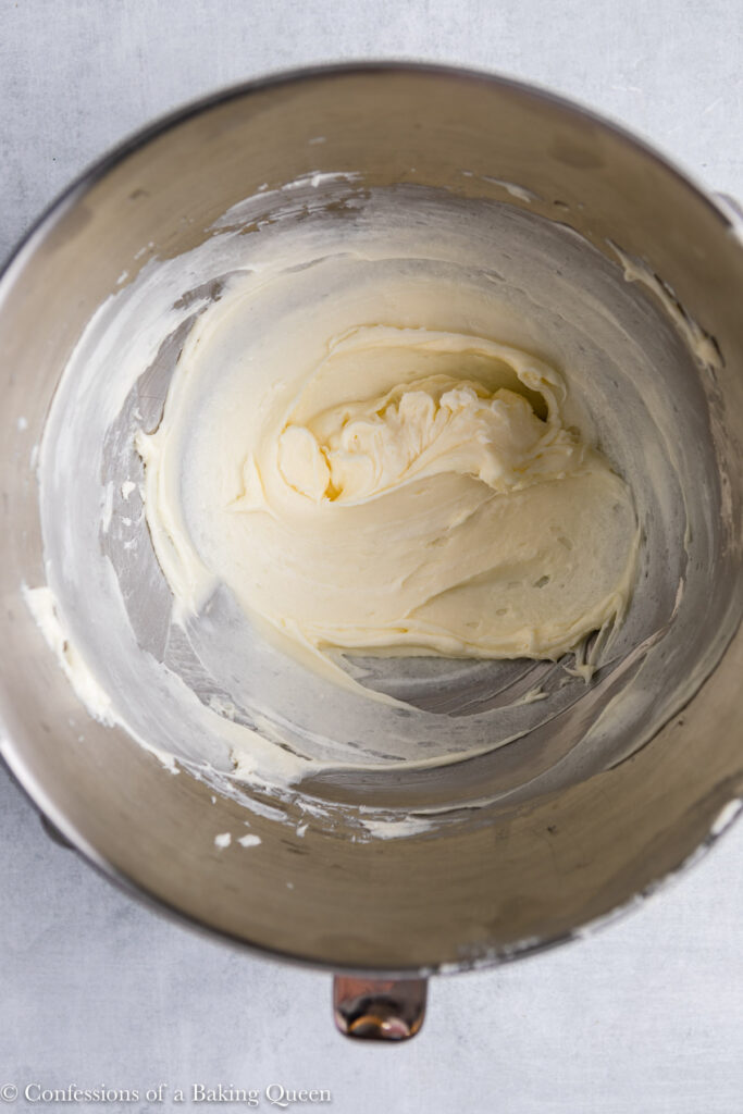 cream cheese and sugar mixed together in a metal bowl on a grey surface