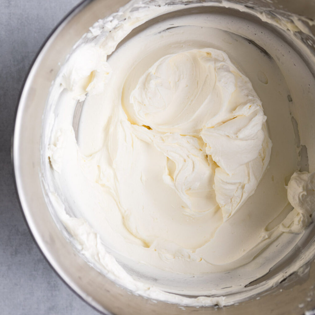 cream cheese whipped cream frosting- in a metal bowl with a wire whisk on a grey surface with a white and black linen
