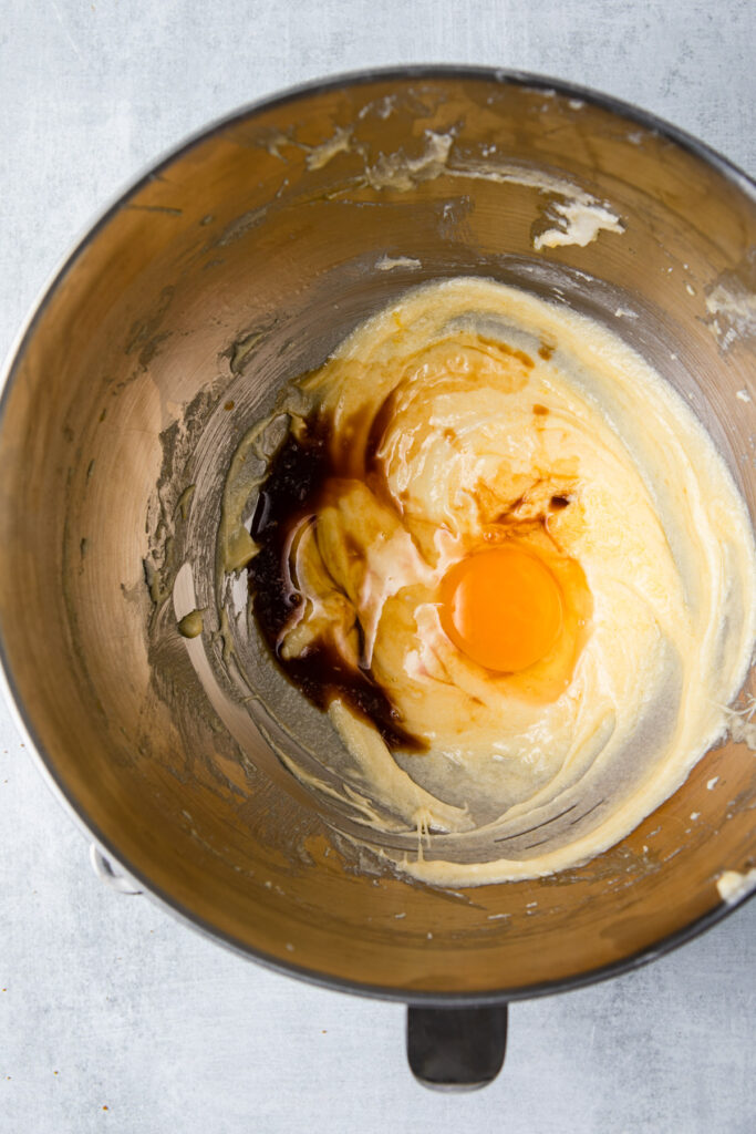 egg and vanilla extract added to butter and sugar mixture in a metal bowl on a grey surface