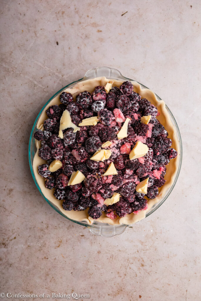 blackberry pie with chunks of butter on top before the top crust is added sitting on a light brown surface