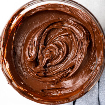 chocolate frosting in a glass bowl on a grey surface with a blue linen