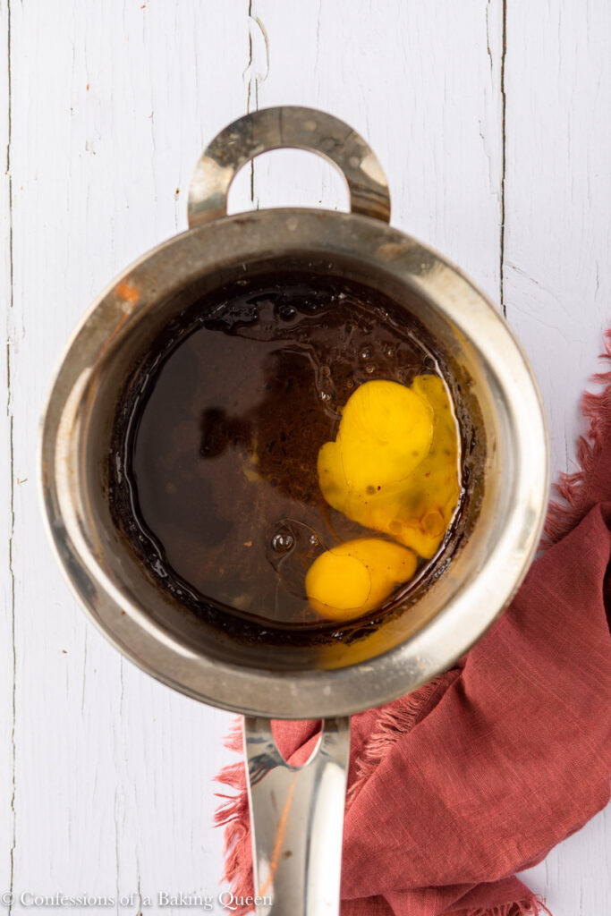 egg and egg yolk added to brownie batter in a metal pot on a white surface with a pink linen