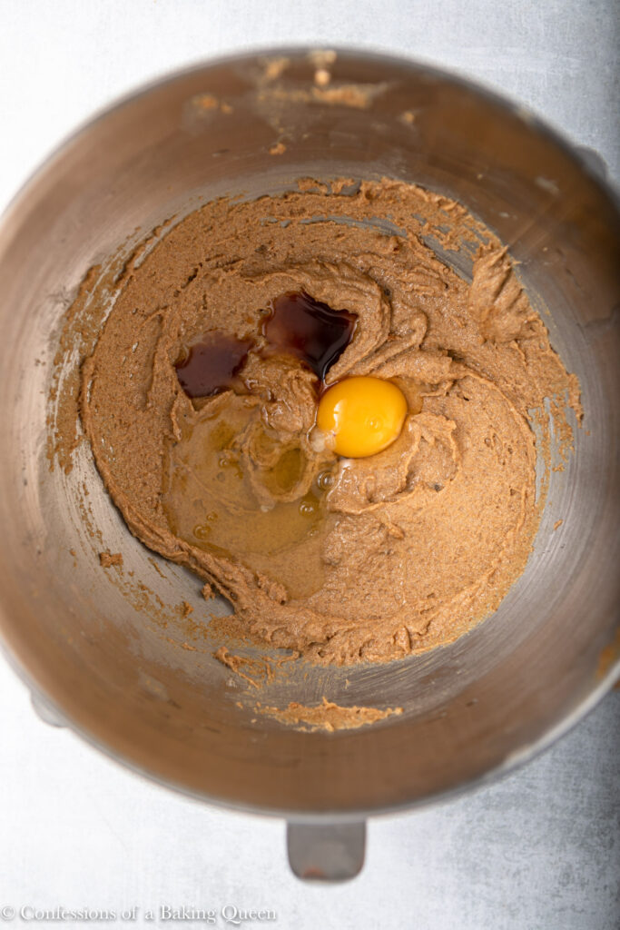 egg and vanilla added to peanut butter, sugar, and butter batter in a metal bowl