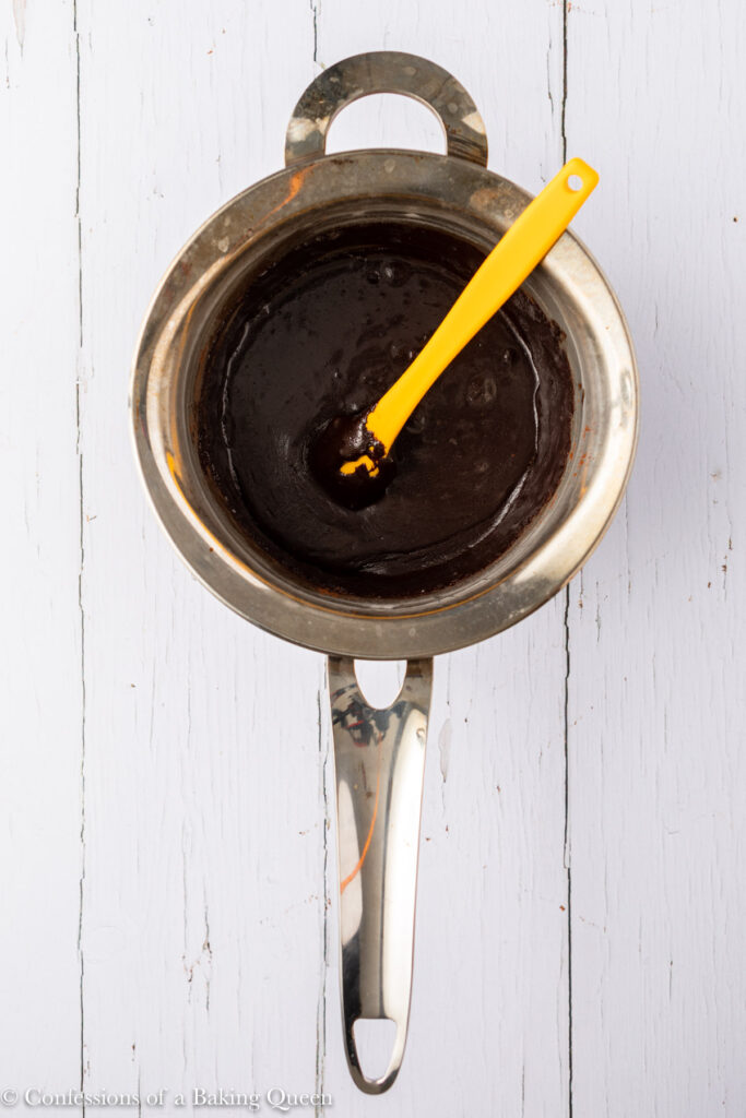 melted butter,sugar, and cocoa powder in a metal pot on a white wood surface