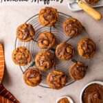 mini pumpkin nutella muffins on a wire rack on a light brown surface with an orange linen, small bowl of nutella, and small plate of pumpkin pie spice