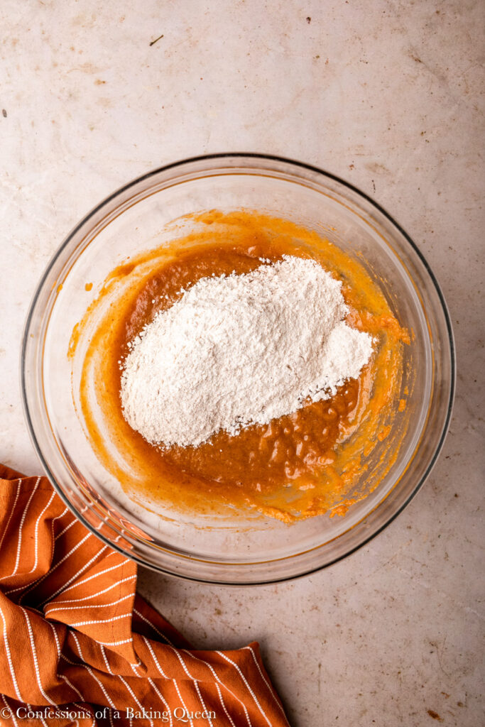 dry ingredients added to wet ingredients for a pumpkin muffin recipe in a glass bowl on an light brown surface with an orange linen