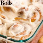 pumpkin cinnamon rolls frosted in a glass dish on a red and brown surface with a wood knife