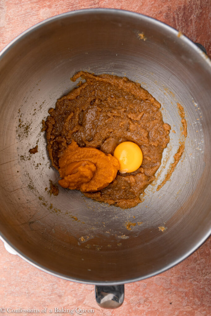 pumpkin puree and egg yolk added to wet ingredients for a pumpkin snickerdoodle recipe in a metal mixing bowl on a reddish brown surface