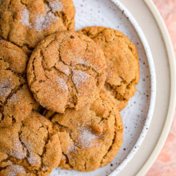 close up of pumpkin snickerdoodles on a white plate on top of a cream plate on a reddish brown surface