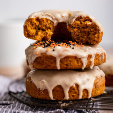 stack of pumpkin cake donuts on a black cooling rack on top of a blue striped towel