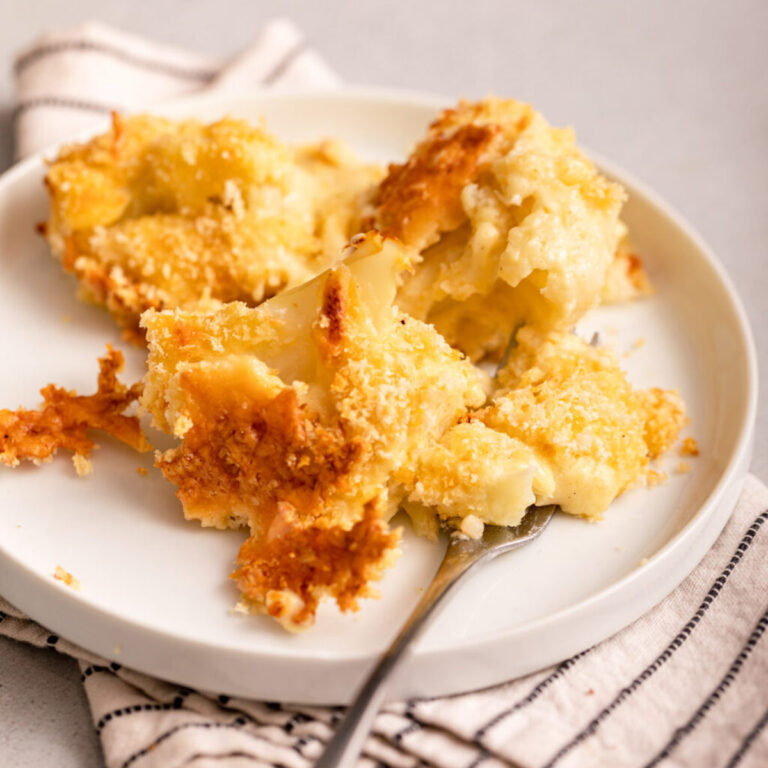 up close of cauliflower cheese on a plate on a larger plate on a light grey surface
