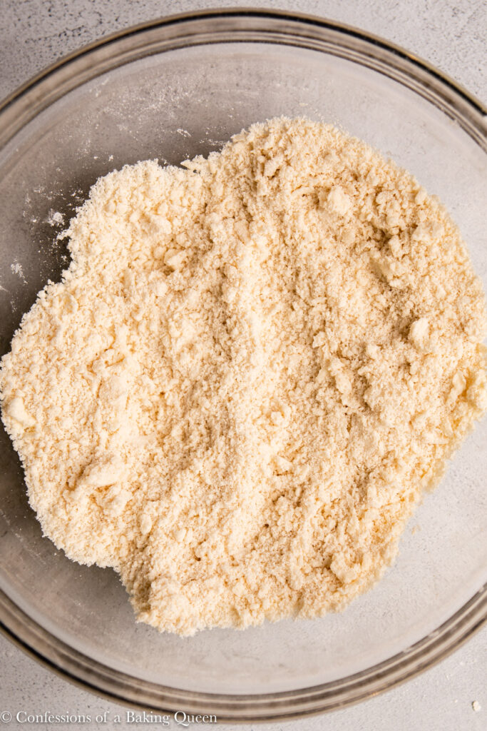 close up of butter and lard rubbed into flour in a glass bowl on an light grey surface