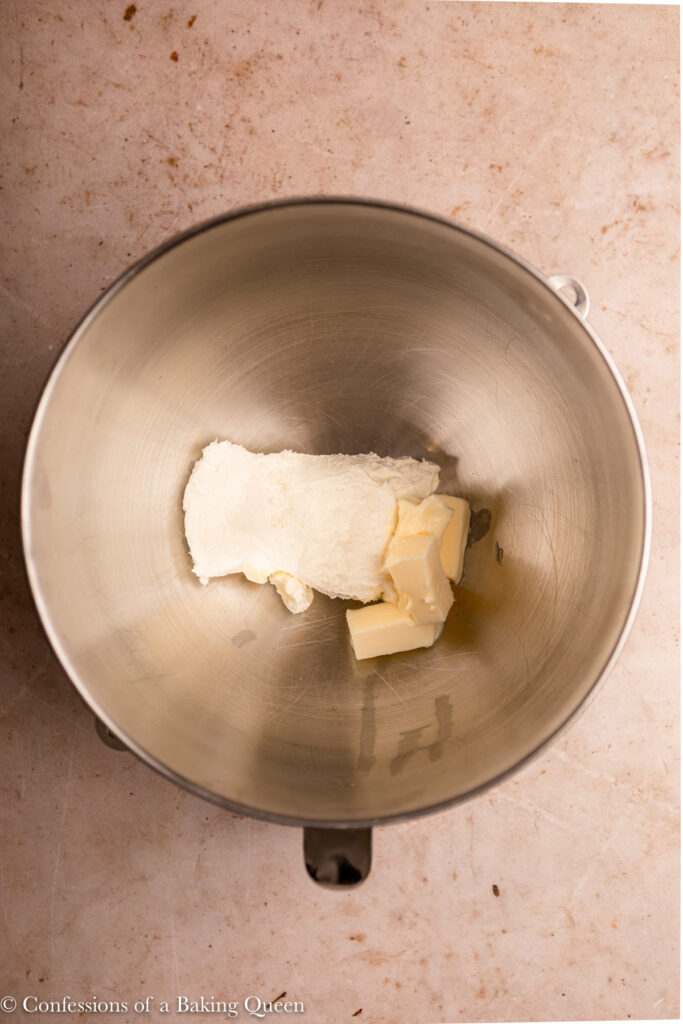 cream cheese and butter in a metal mixing bowl on a light brown surface