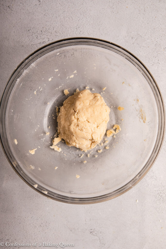 flaky pie crust pressed into a ball in a glass bowl on a light grey surface