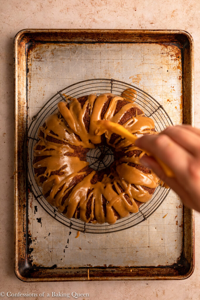 toffee sauce drizzled on top of an apple bundt on a wire rack on a sheet pan on a light brown surface