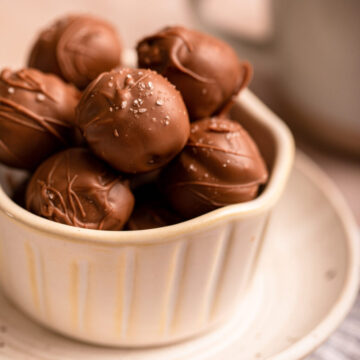 sea salt chocolate truffles in a small bowl on a small plate on a light brown surface with a cup of coffee in the background