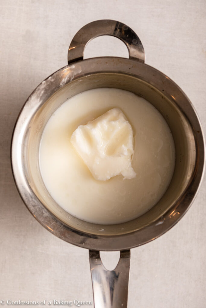 lard, water, and milk in a small pot on a light grey surface