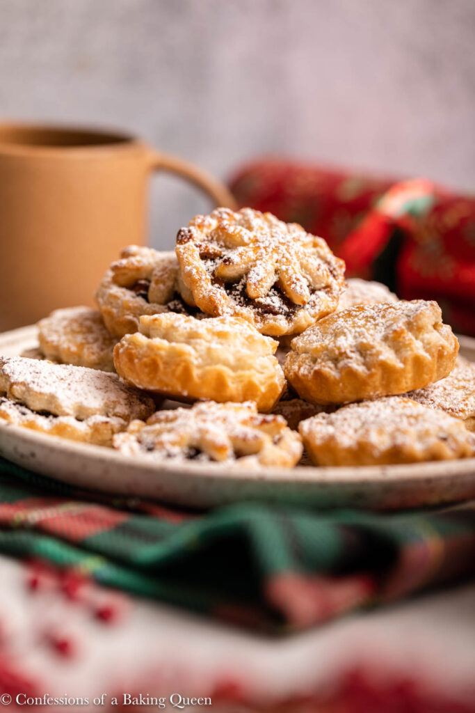 mince pies on a plate next to Christmas crackers and a cup of coffee on a light grey surface