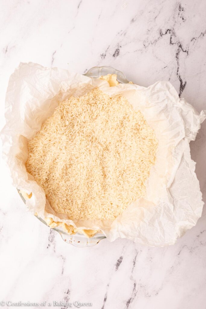 pie crust filled with parchment and rice sitting on a white marble surface