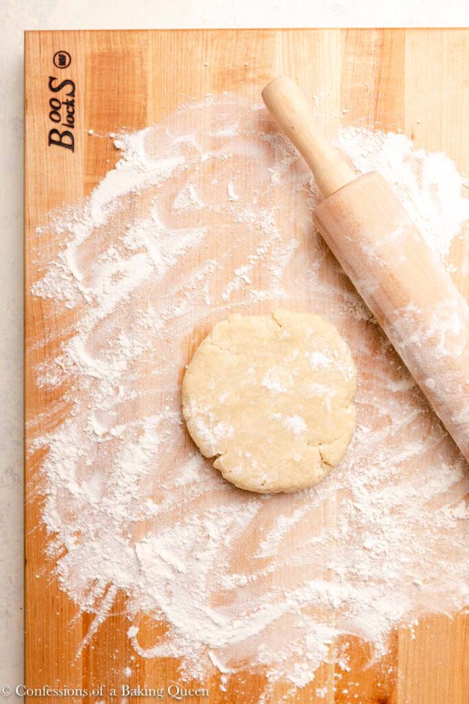 pie dough disc on a floured board with a floured rolling pin all on a white surface