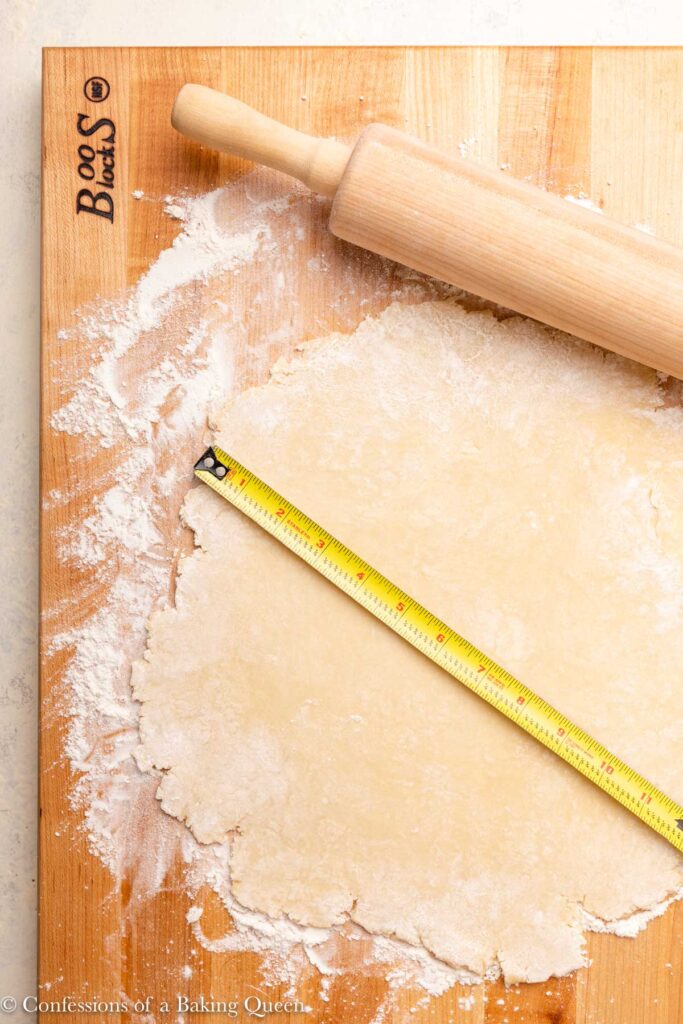 pie dough rolled into 12 inch circle measured with a tape measure on a floured wood board with a rolling pin
