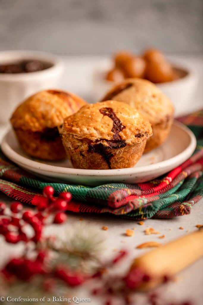 three pork pies on a small plate next to christmas decorations on a light grey surface