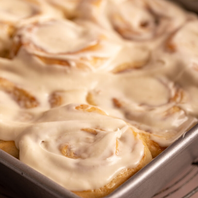cream cheese frosted cinnamon rolls in a pan next to a knife and linen