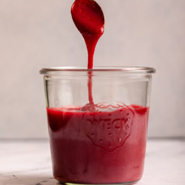 spoon dripping raspberry coulis back into the glass jar on a marble surface
