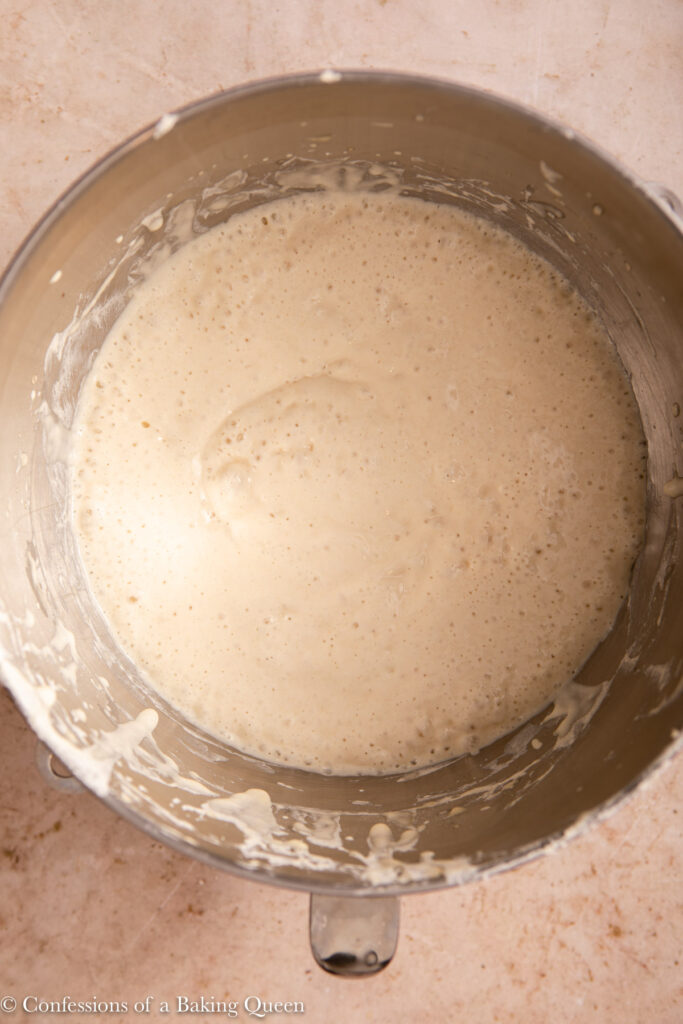 crumpet batter after resting in a large metal bowl on a light brown surface