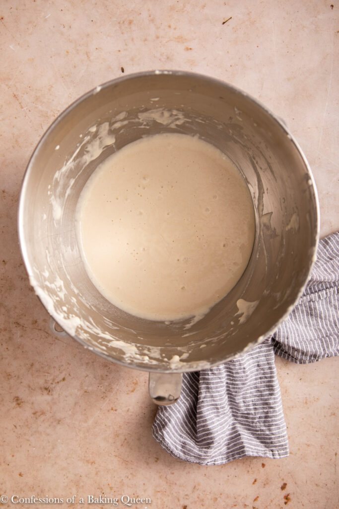 crumpet batter in a metal bowl on a light brown surface with blue linen