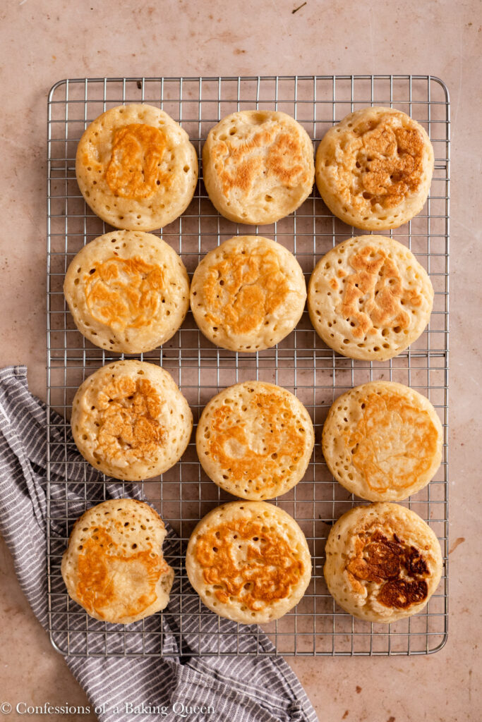 crumpets cooling on a wire rack on top of a blue linen on a light brown surface