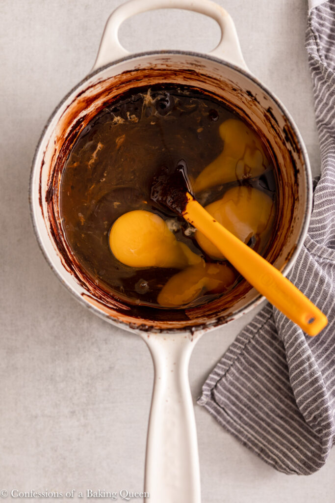 egg and egg yolk added to brownie batter in a small pot on a light grey surface with a blue linen
