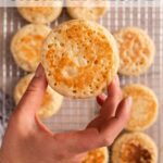 hand holding a crumpet above a rack of more crumpets on a light brown surface