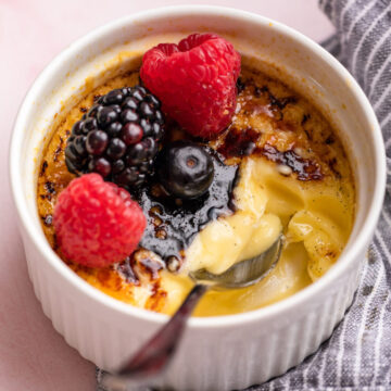 half eaten creme brulee with berries and a spoon on a pink surface and a blue linen