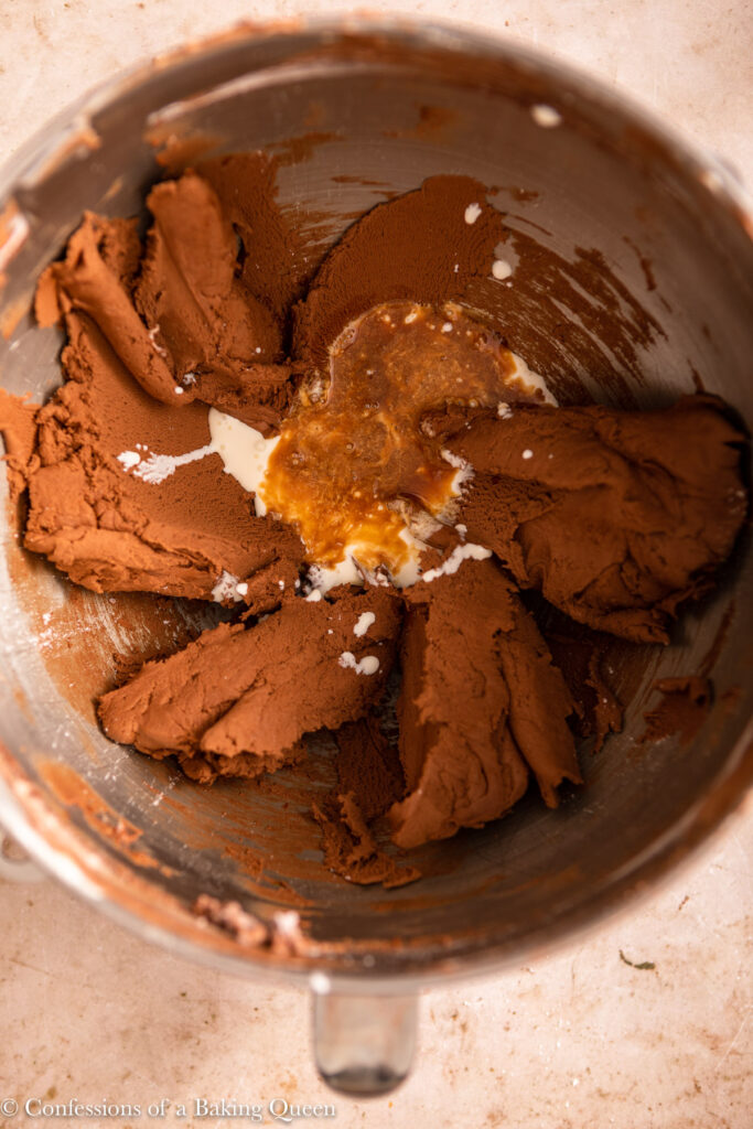 heavy cream and vanilla added to chocolate buttercream in a metal bowl on a light brown surface