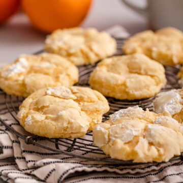 orange crinkle cookies on a wire rack on top of a linen with oranges in the background